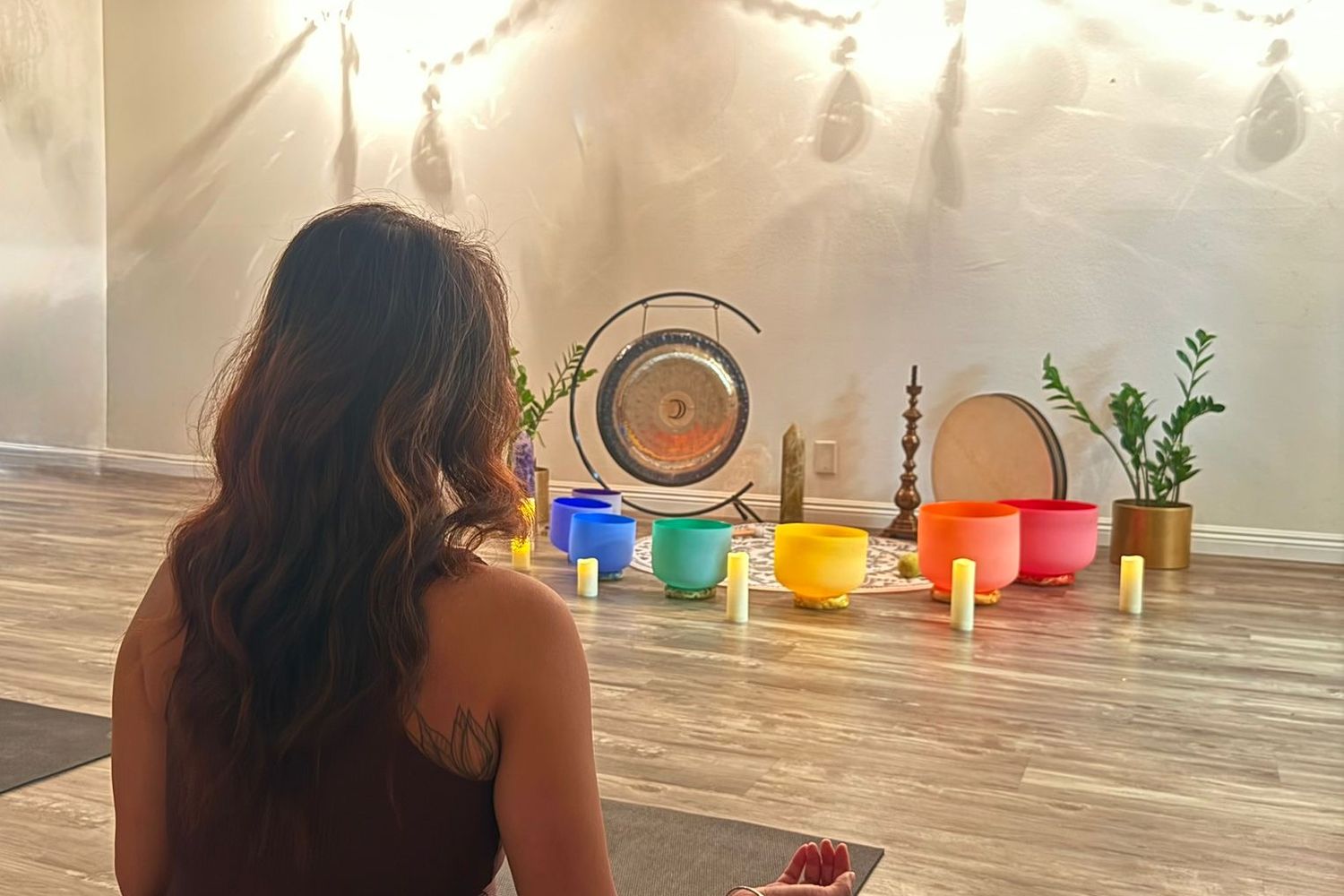 A woman seated cross-legged on the floor of the Healing Sanctuary facing the gong and bowls