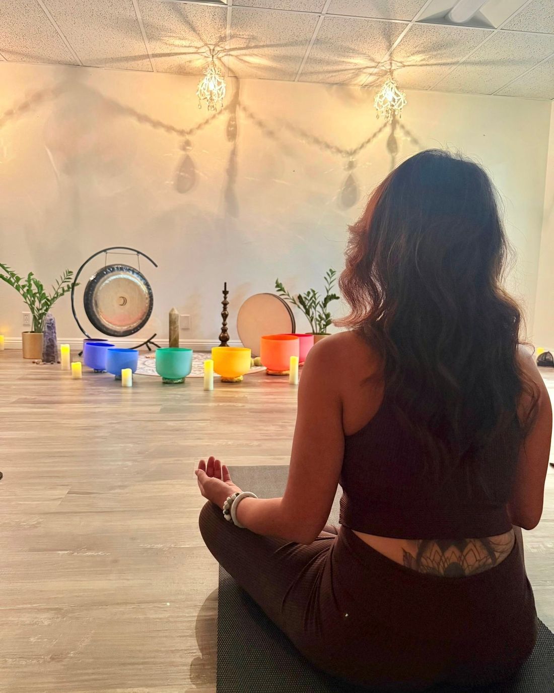 A woman seated on the floor of the Healing Sanctuary beneath warm string lights